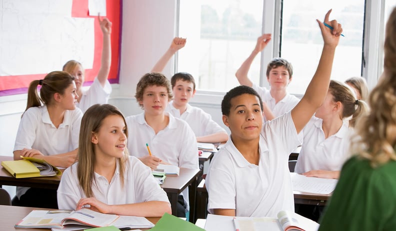 High school children in class with arms raised 